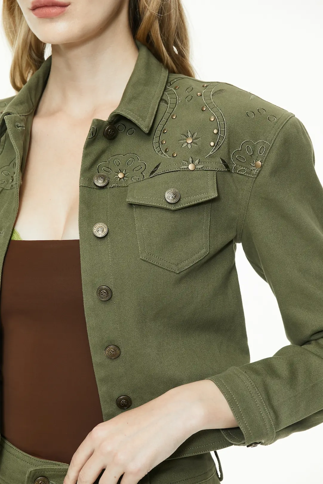 Close-up shot showing the detailed western yoke, metallic studs, button closure, and flap chest pocket on the olive green cropped jacket.