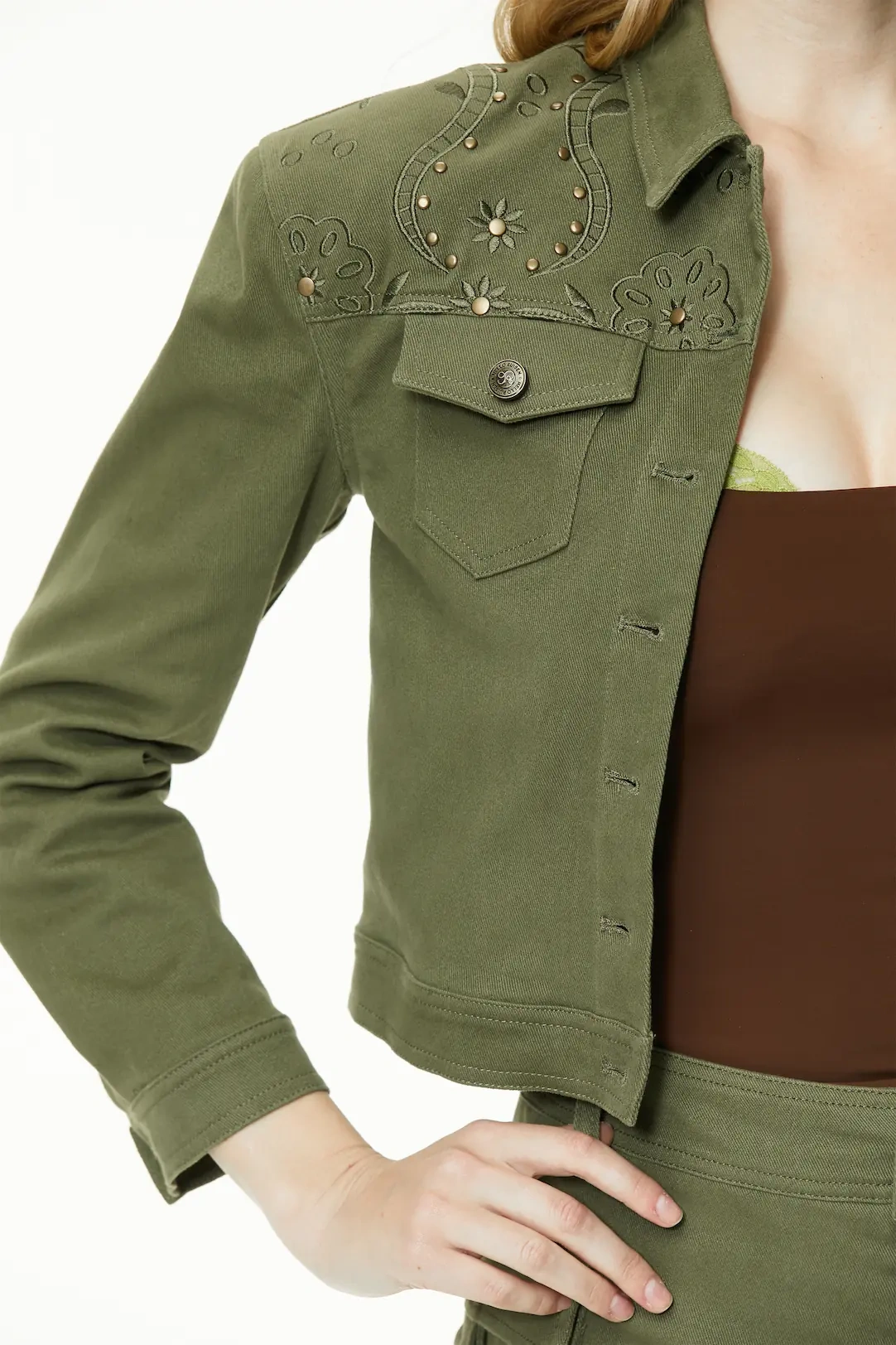 Detailed side view highlighting the shoulder stud design, point collar, and sleeve cuffs on the olive green cropped jacket.