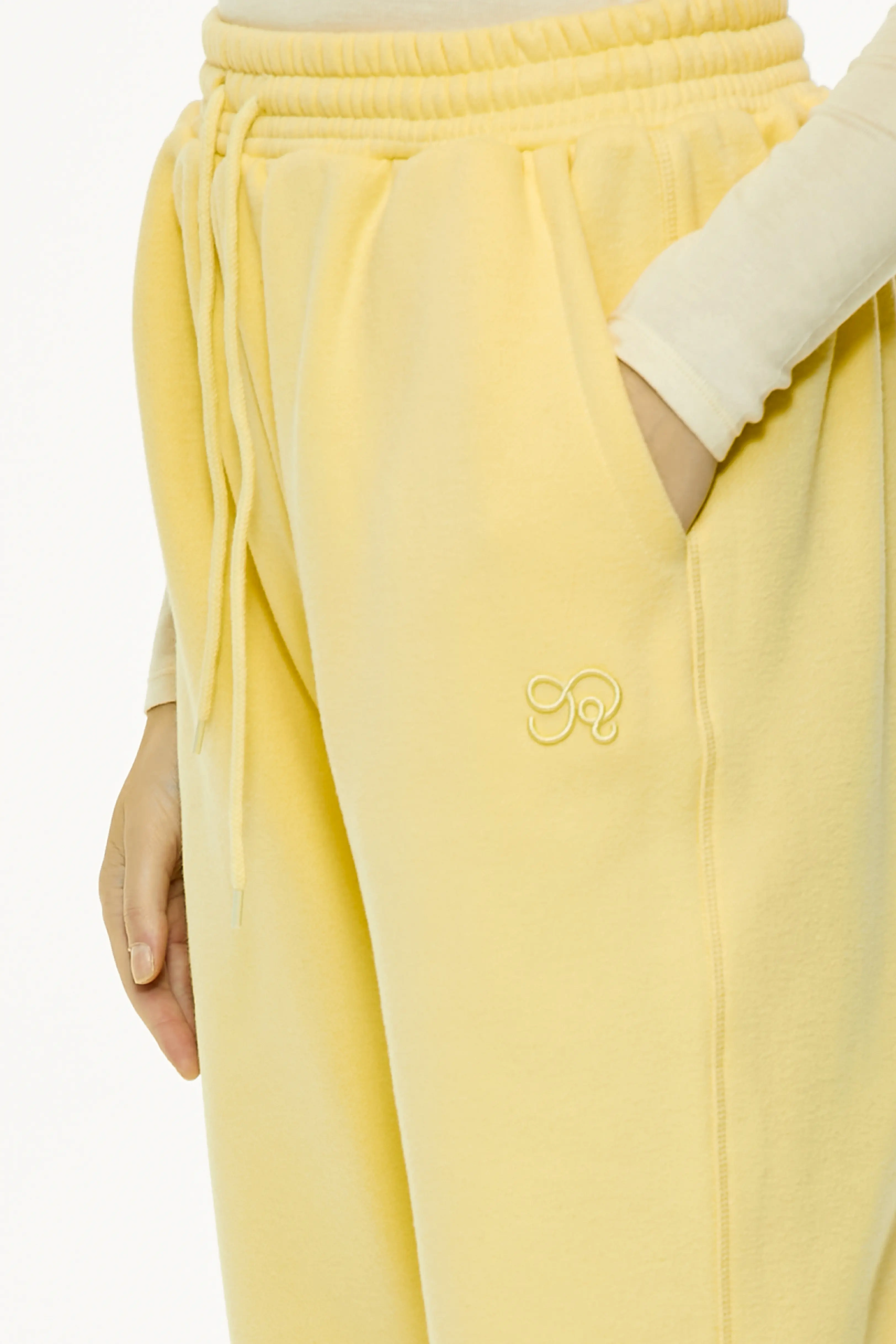 Close-up of yellow relaxed fit sweatpants featuring side pocket and embroidered logo