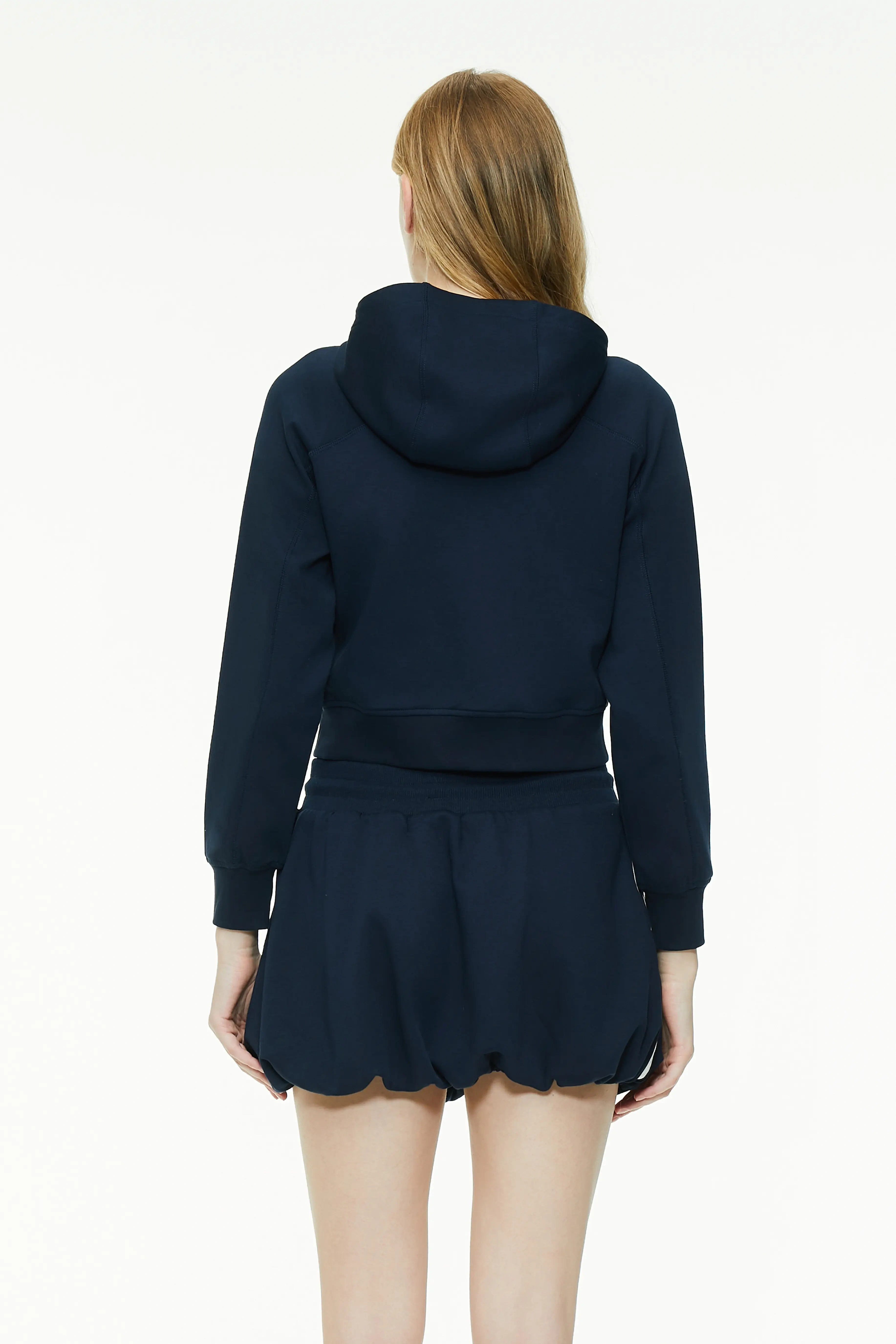 Back view of a navy blue cropped zip-up hoodie showing the hooded design, back seam, and relaxed fit hem.
