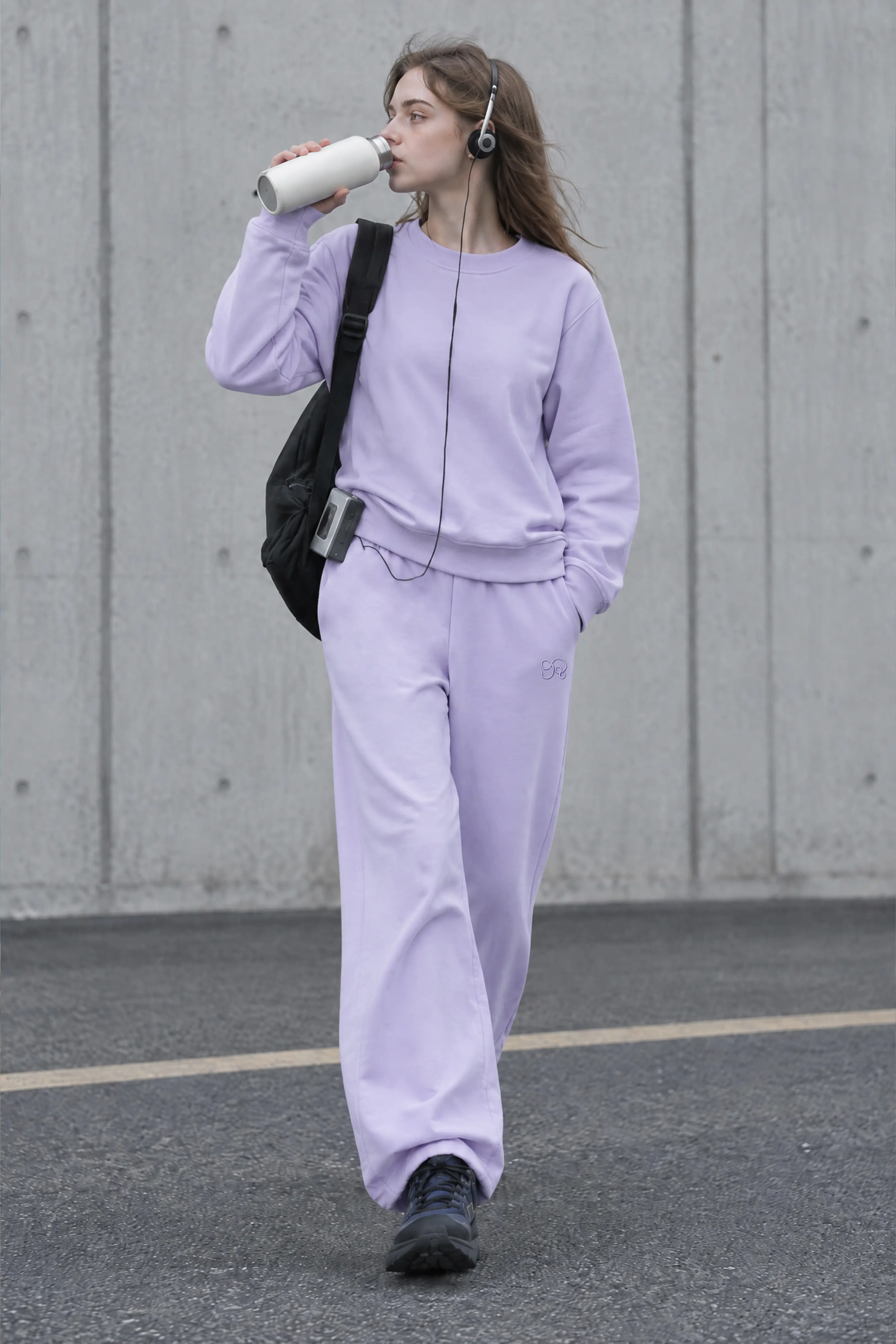 Light purple wide leg sweatpants with matching hoodie and black backpack in urban setting