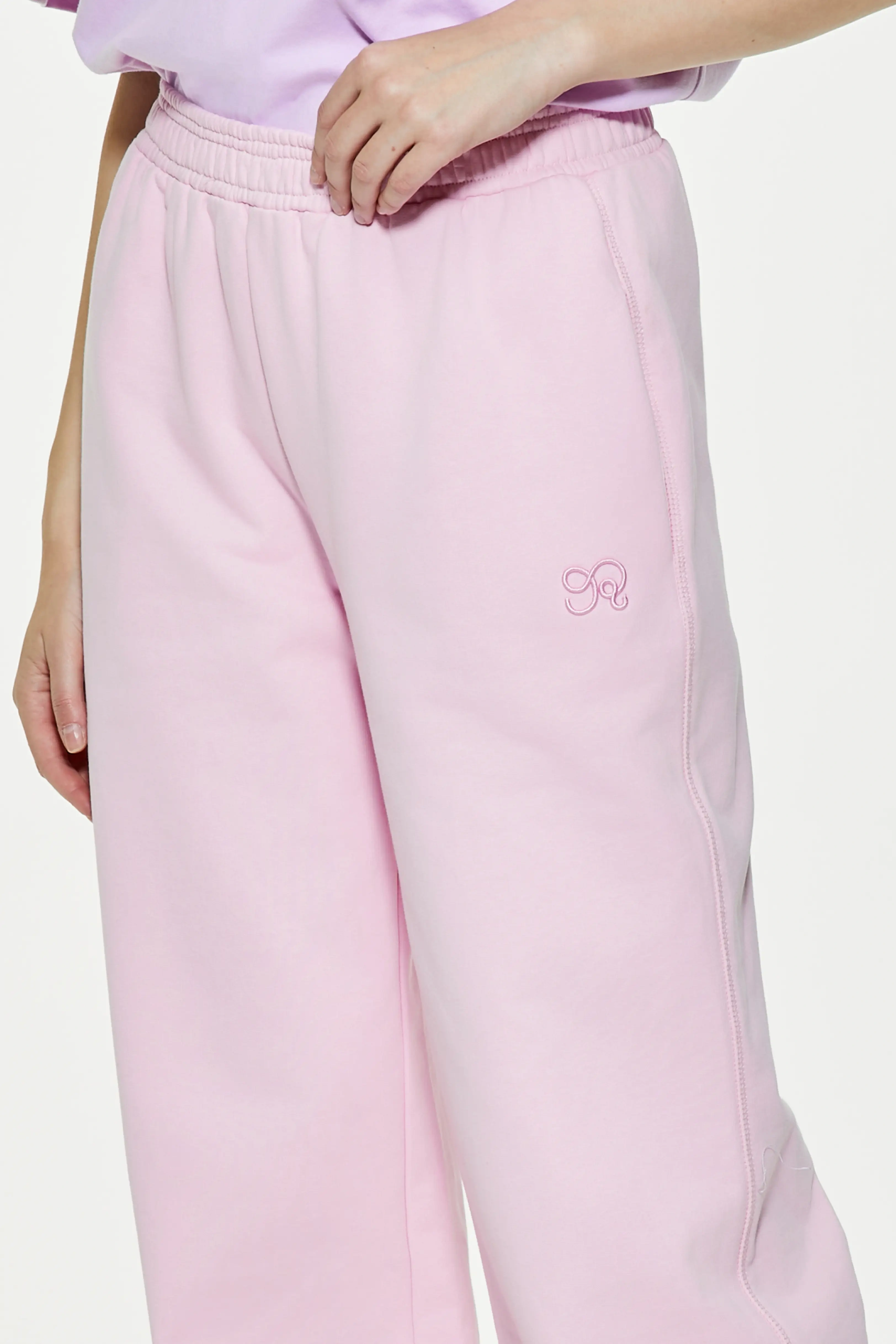 Close-up of light pink wide leg sweatpants highlighting small embroidered logo on hip