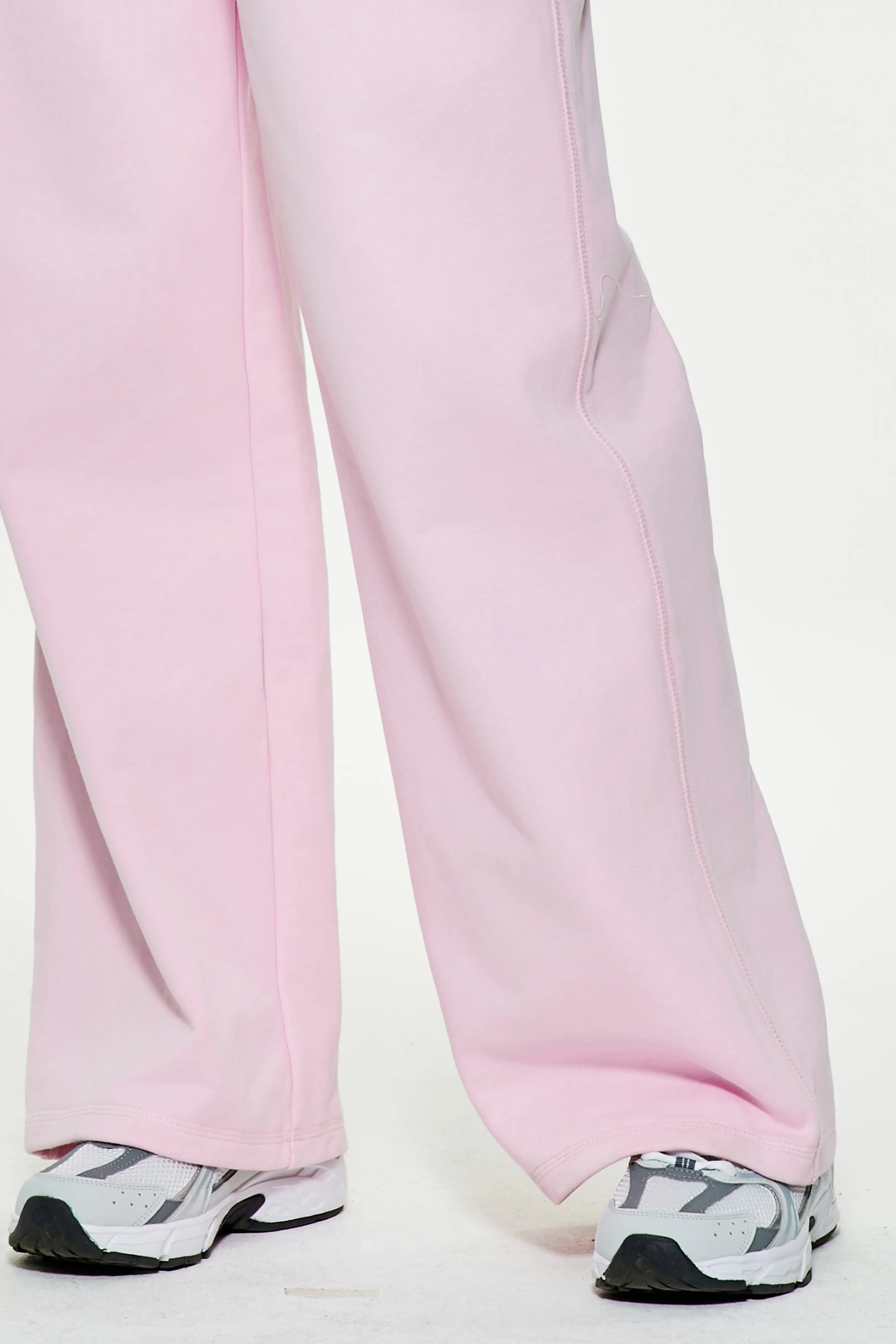 Close-up of light pink wide leg sweatpants showing loose hem and athletic shoes