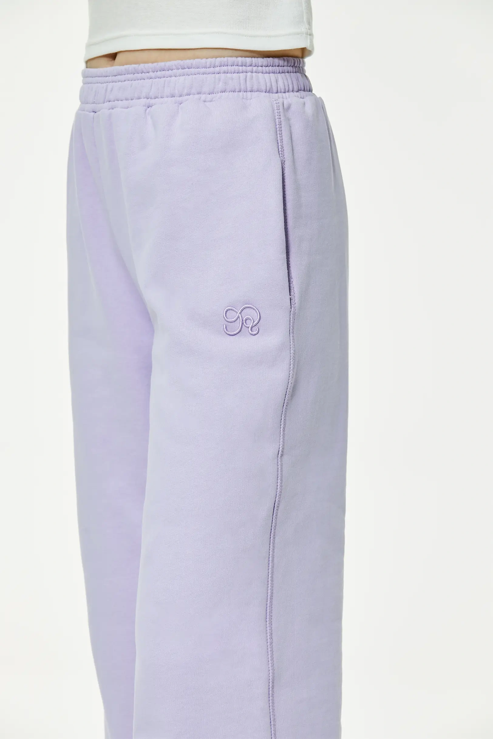 Close-up of light purple wide leg sweatpants highlighting small embroidered logo near pocket