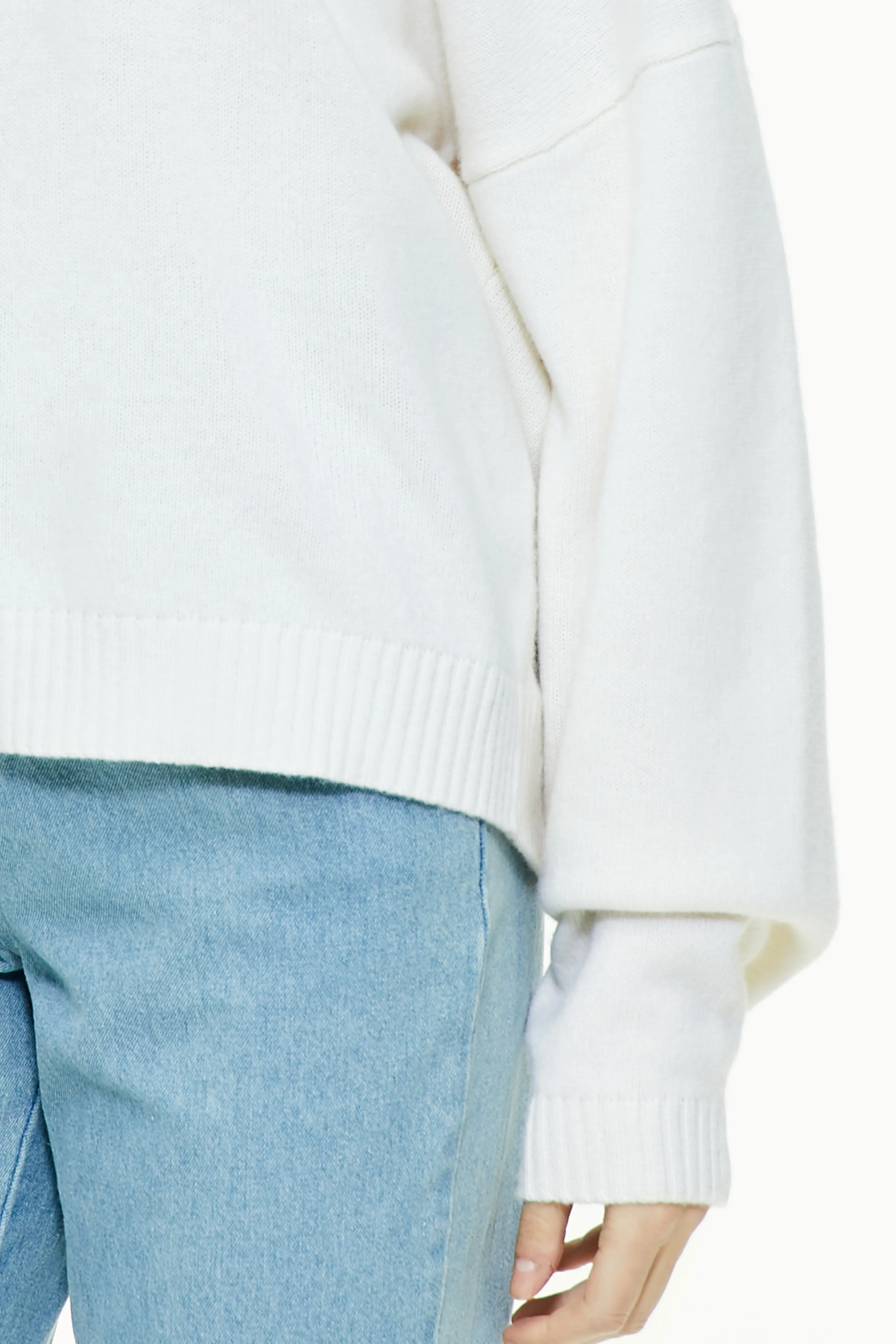 Close-up showing the ribbed hem and cuff detail of the white turtleneck sweater