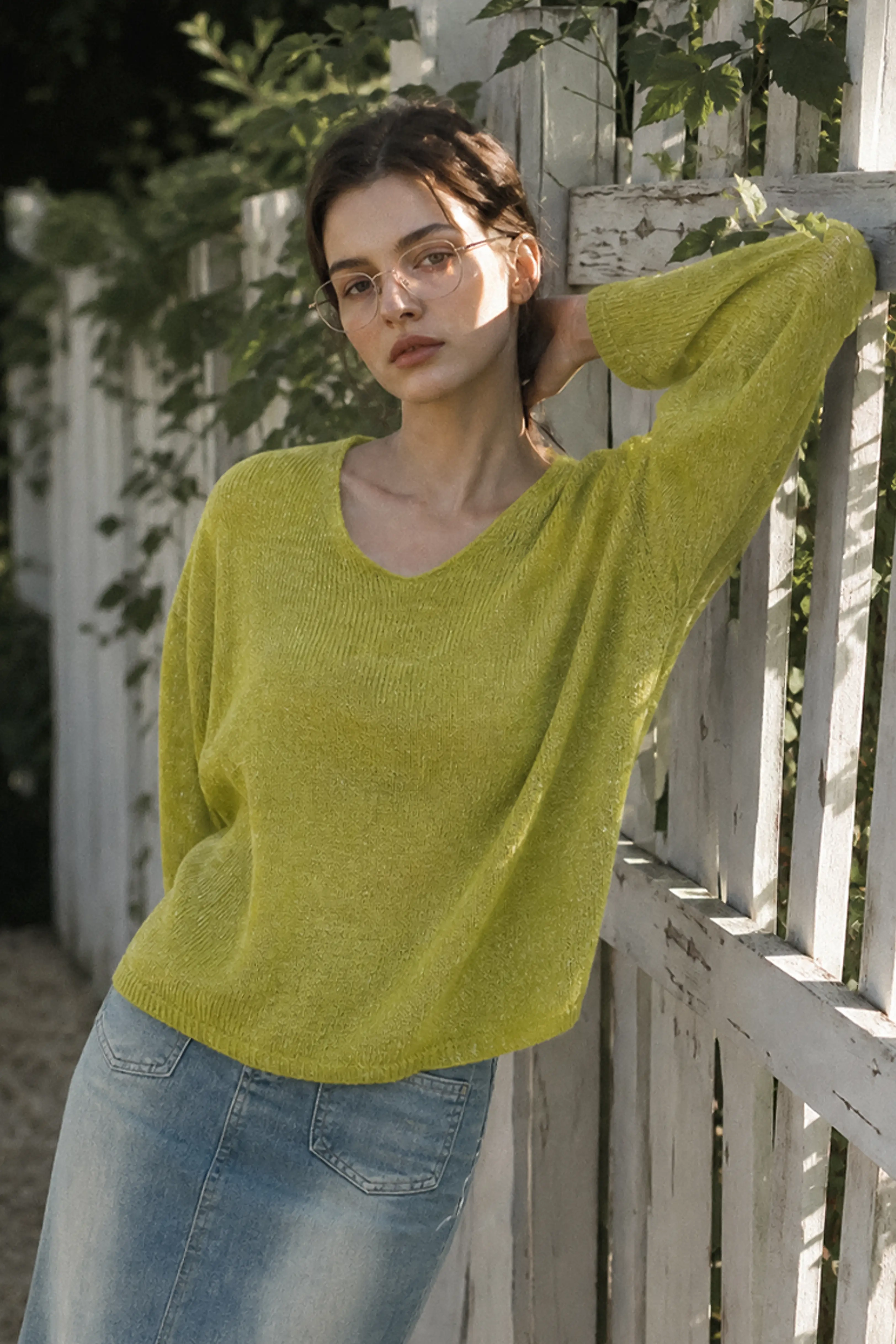 Chartreuse loose knit sweater paired with denim trousers in an outdoor street setting
