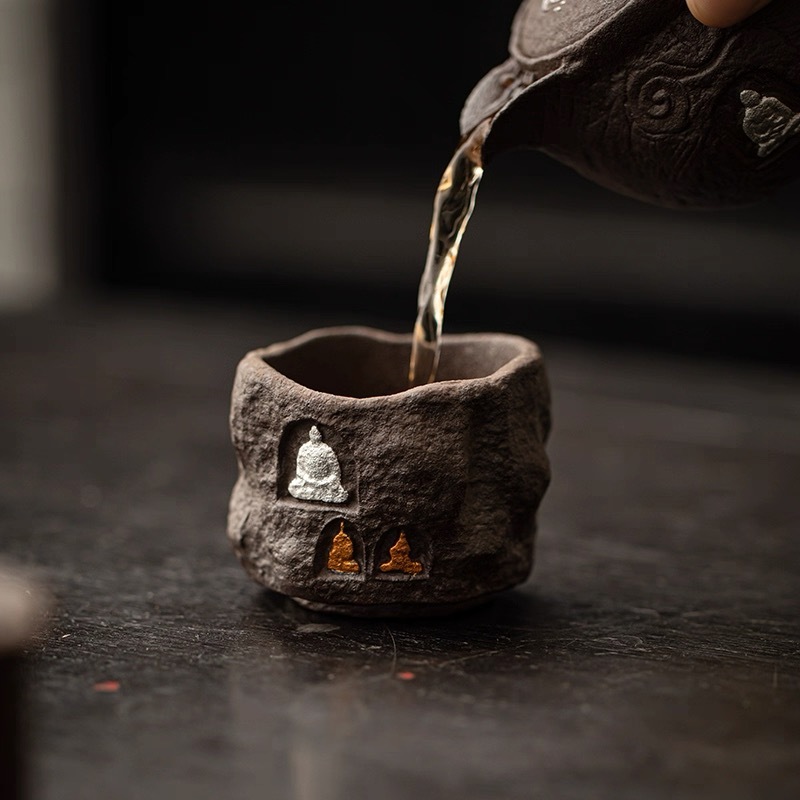 Handcrafted Dunhuang-inspired tea vessel by Eartivo; the "Stone Sanctuary" presents an arched grotto aesthetic with unrefined mineral-rich clay, where the gold and silver icons naturally mature and oxidize over time.