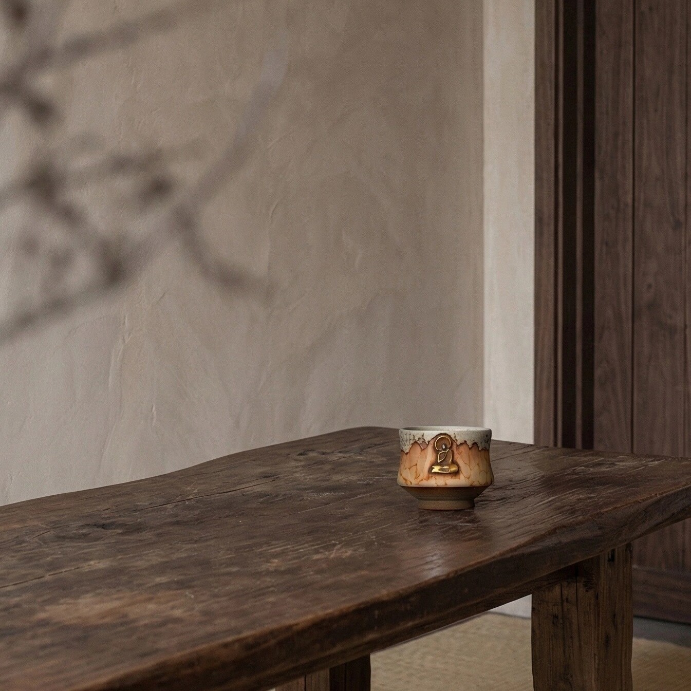 The Abstract Ascent — Shino wood-fired pottery cup with gold Buddha figure on aged wood table, modern zen interior accents in a minimalist room