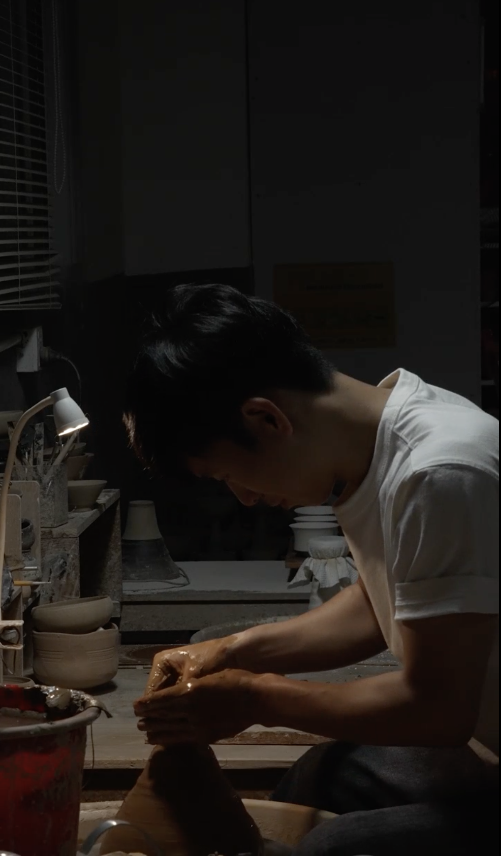 Ceramic artist hand-throwing clay on a pottery wheel in a studio &mdash; the making process behind handmade ceramic art and unglazed stoneware