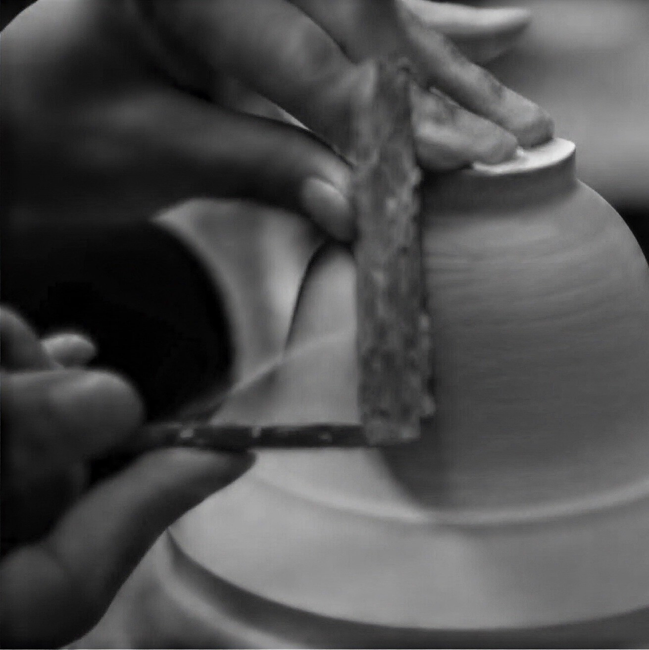 Close-up of hands trimming a wheel-thrown ceramic vessel &mdash; the forming process that gives handmade pottery decor its coarse-grained texture and surface information