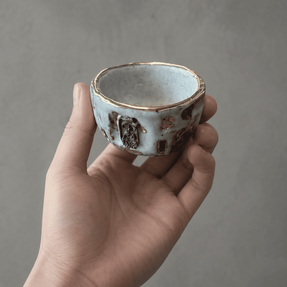 A profound moment of ritual as tea interacts with Eartivo "The Resilient Gold"; the raw Rock-Mineral base meets the handcrafted gold icon, representing the "90% finished vessel"—completed by your presence and a smooth, tea-infused "patina"