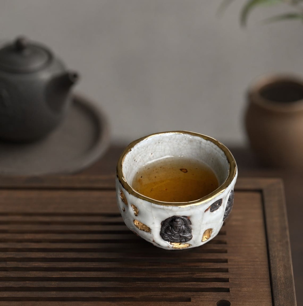 A profound moment of ritual as tea interacts with Eartivo "The Resilient Gold"; the raw Rock-Mineral base meets the handcrafted gold icon, representing the "90% finished vessel"—completed by your presence and a smooth, tea-infused "patina"