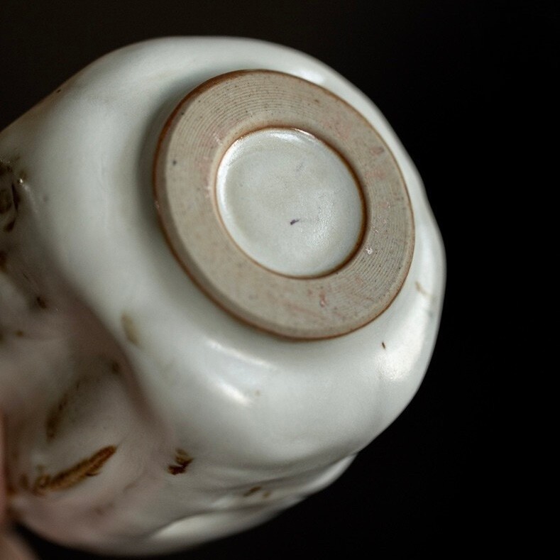 A bottom view of Eartivo "The Snow-Veiled Sanctuary" vessel, showcasing the contrast between the rough-hewn Rock-Mineral side and the handcrafted gold-covered Buddha; designed to naturally develop a deep, rich "patina" over time through daily use.