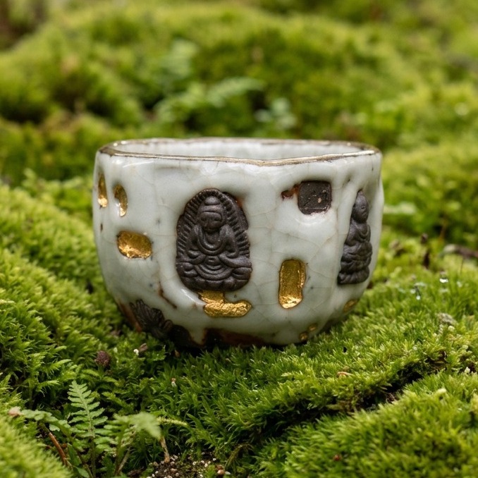 A tactile sensory experience of a handcrafted ceramic teacup with Buddha reliefs and gold kintsugi details, nestled in lush green moss. Embodying high ground energy and the slow living lifestyle through the rituals of tea.
