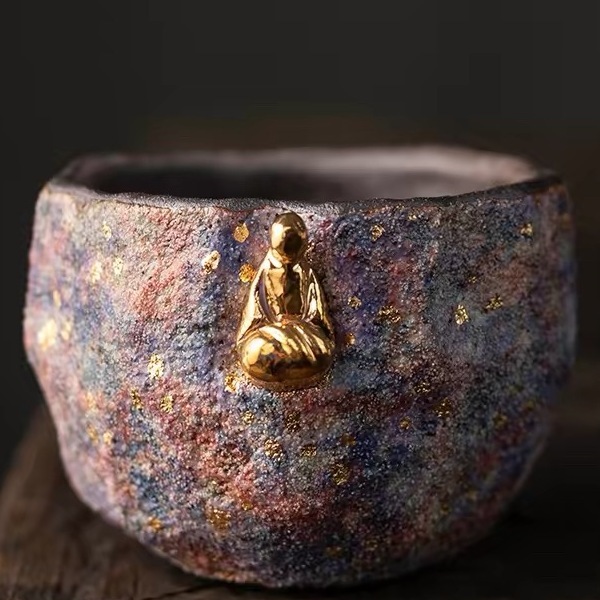 Rock-mineral clay "Cosmic Bloom" tea cup with a small detailed gold meditator figure near the center, showcasing its unique multi-colored galaxy finish.