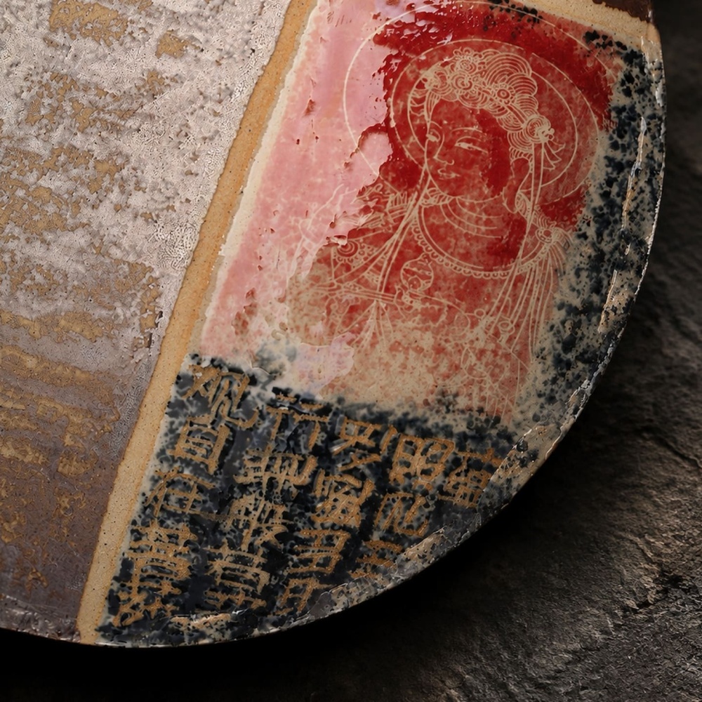 Macro detail of the Dharma & Ash ceramic plate, highlighting the fine hand-painted red Buddha portrait and ancient Buddhist calligraphy set against aged ceramic glaze.