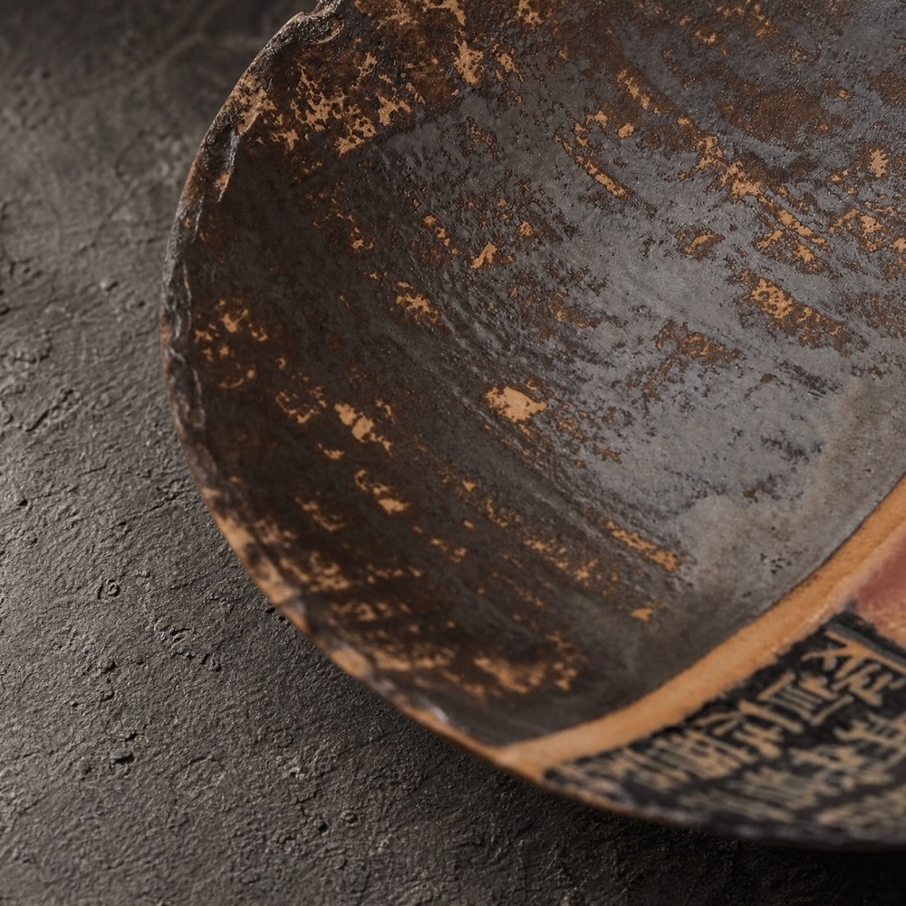 Close-up angled view of the Dharma & Ash stoneware plate, showcasing the tactile aged dark glaze and weathered mineral-fired surface textures.