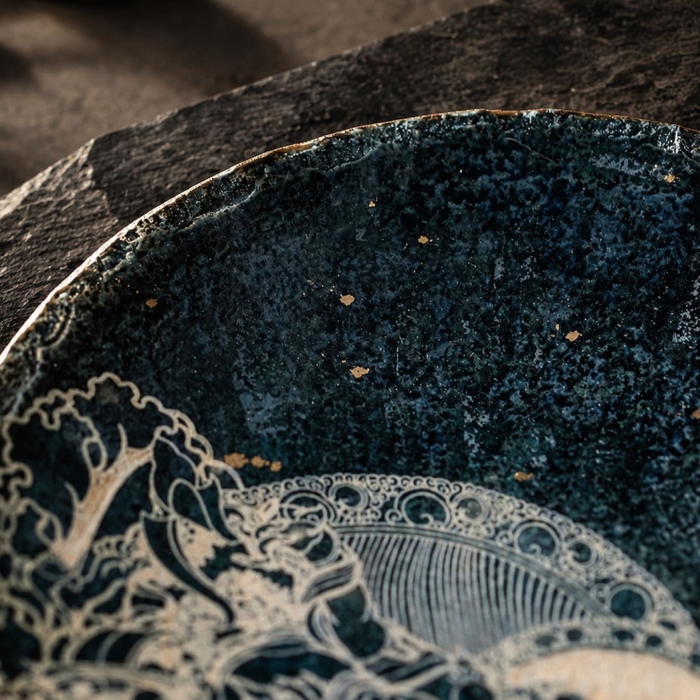 Macro close-up of the Midnight Deity artisan plate, capturing the tactile texture of delicate hand-carved deity linework paired with luminous scattered gold fleck craftsmanship.