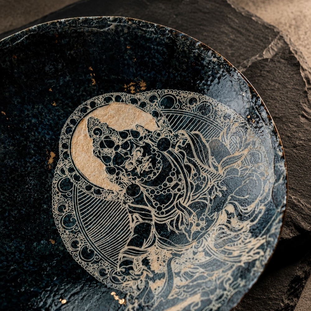 Macro close-up of the Midnight Deity artisan plate, capturing the tactile texture of delicate hand-carved deity linework paired with luminous scattered gold fleck craftsmanship.