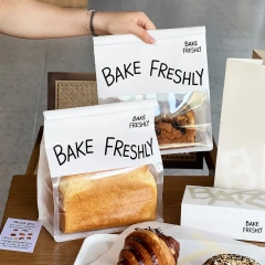 Two printed toast packaging bags with clear windows held over a bakery table