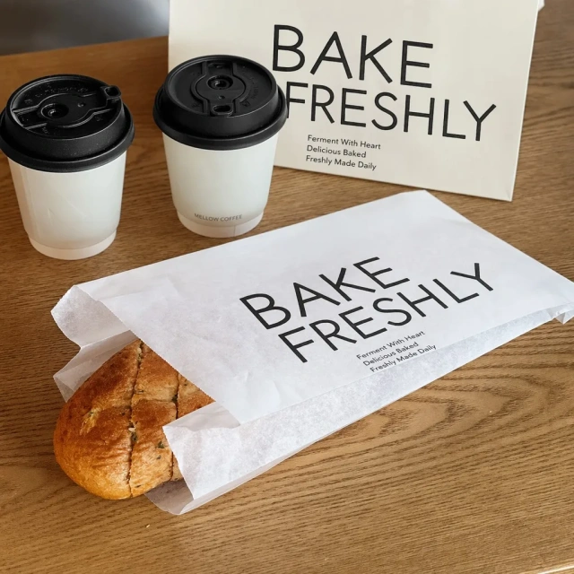 Flat greaseproof bakery paper bag with bread roll and two paper coffee cups