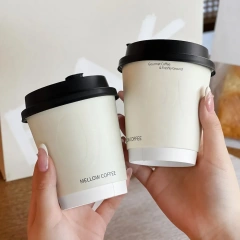 Two double-wall paper coffee cups with black lids held up in a bakery