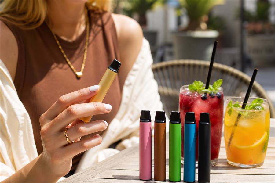 adult holding a disposable vape at a cafe table