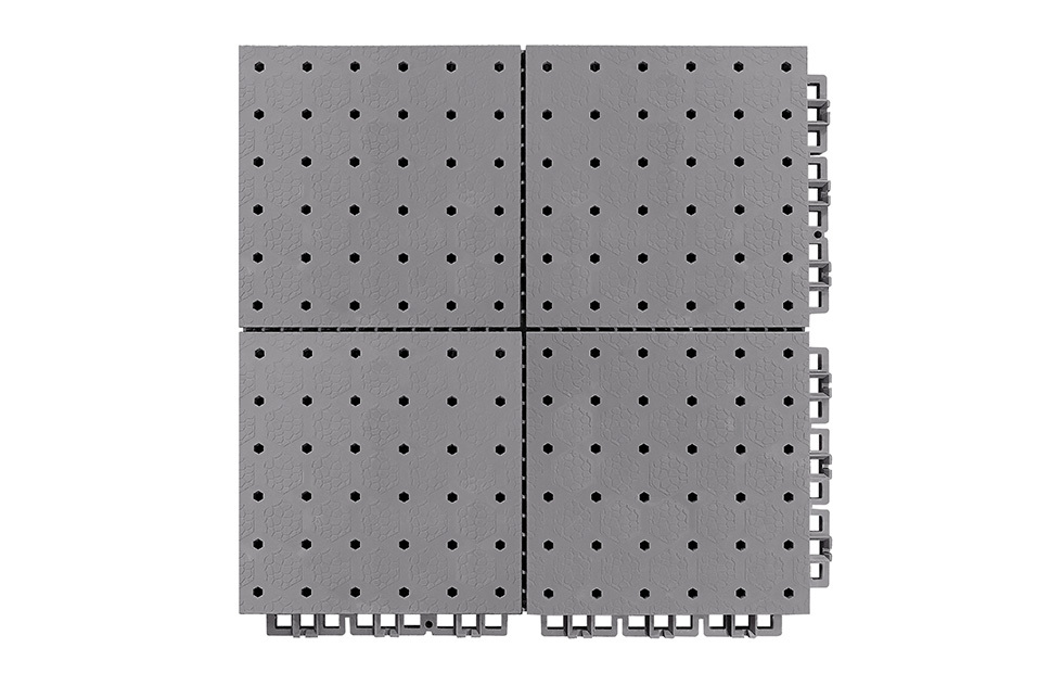 Top-down view of a 305×305×13mm thermoplastic rubber sports flooring tile showing the thickened hexagonal surface texture and hexagonal through-hole drainage perforations, in grass green, as used on outdoor school sports courts and municipal fitness project surfaces.