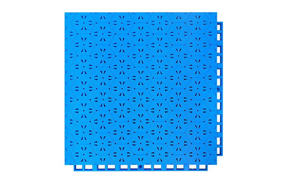 Top-down view of a 305×305×14mm thermoplastic rubber safety flooring tile showing the family hexagonal surface pattern and non-slip texture surface, with visible drainage holes and auxiliary drainage trenches, designed for anti-slip performance on both outdoor sports fields and kindergarten activity areas.