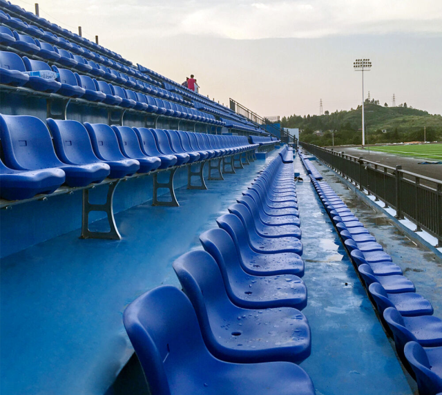 Eco-M HDPE blow molded stadium seats in wall installation configuration mounted to vertical riser faces on a bleacher structure, showing mounting bracket interface and seat positioning