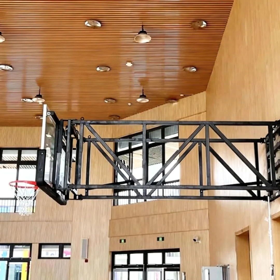 FIBA wall mounted basketball stand installed in high school gymnasium or university training hall showing side-fold backstop in deployed play position and retracted nearly-flat wall storage profile, multi-sport court floor area preserved without floor post footings, and institutional facility wall-mount integration