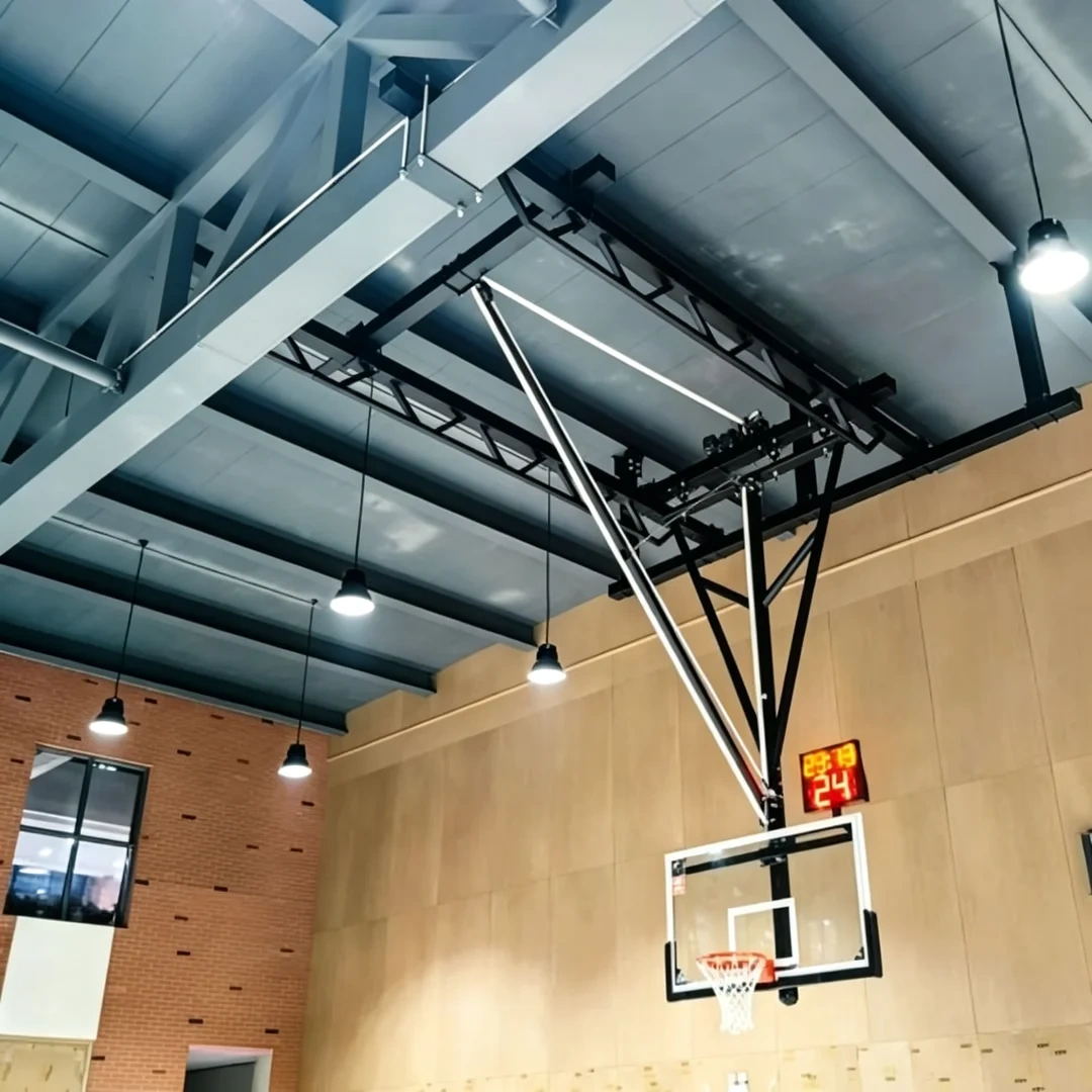 Ceiling suspended backstop in smooth forward fold actuation position showing folding mechanism joints, fold trajectory from play position to stored overhead position, and structural frame geometry during multi-sport court conversion cycle