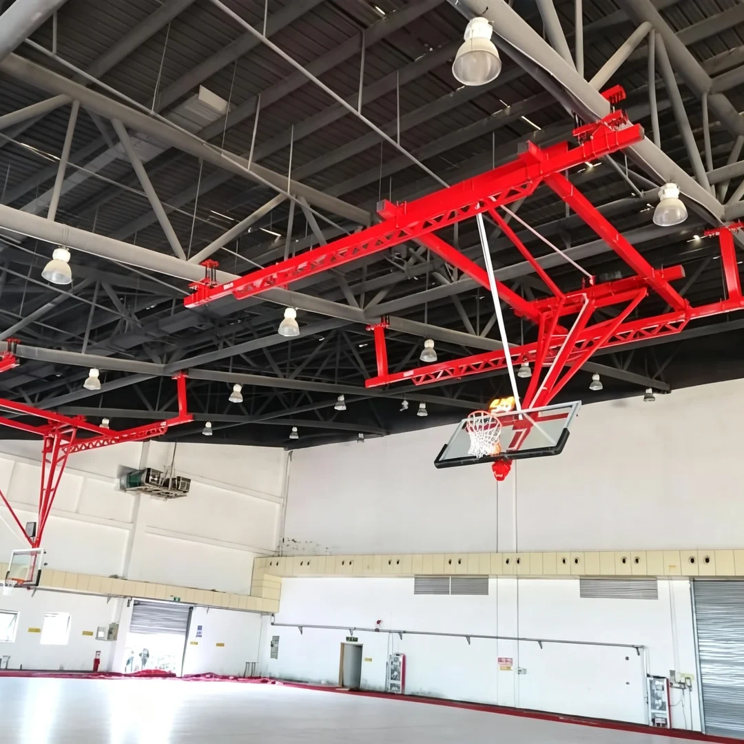 Close-up detail of ceiling suspended backstop showing heavy diagonal sway bracing connection to overhead structural mounting, diagonal brace geometry, pre-welded frame joint, and powder-coat surface finish on structural tubing at basketball arena ceiling interface