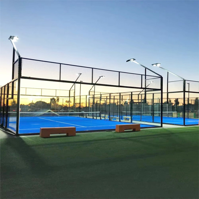 Panoramic padel court H001 installed at outdoor hotel or sports club facility showing complete hot dip galvanized steel frame structure, 12mm tempered glass panels, EN 12193 LED floodlight array, and court positioned within coastal or resort landscape site context