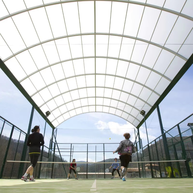 Panoramic padel court with simple roof H007R complete isometric view showing 20×10m FIP-compliant court layout, hot dip galvanized heavy structural steel frame, integrated simple roof steel structure on court foundation, 12mm tempered glass EN 12150-1 panoramic panels, and LED floodlight array in covered outdoor sports club or resort context