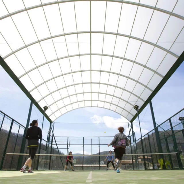 Panoramic padel court with simple roof H007R complete isometric view showing 20×10m FIP-compliant court layout, hot dip galvanized heavy structural steel frame, integrated simple roof steel structure on court foundation, 12mm tempered glass EN 12150-1 panoramic panels, and LED floodlight array in covered outdoor sports club or resort context