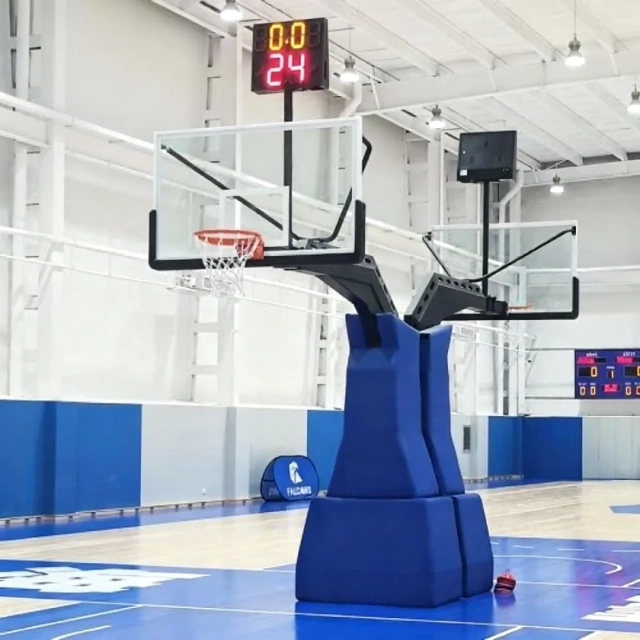 High-magnification detail of 180×105cm × 1.2cm transparent tempered glass backboard panel matrix and solid steel flex rim interface on FIBA-approved inground basketball hoop, with protective frame shielding and custom padding graphics visible.