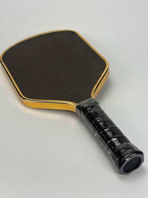 Close-up detail view showing the fitment of the TPU tape guard onto the handle joint of the TITANIUM Pickleball Paddle, highlighting the custom logo interface.