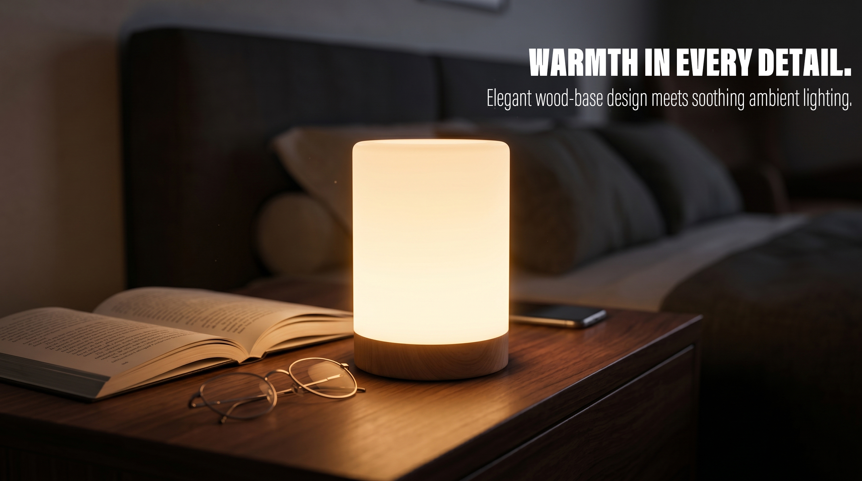 A glowing cylindrical table lamp with a wood base placed on a bedside table next to an open book and glasses in a warm, cozy bedroom setting