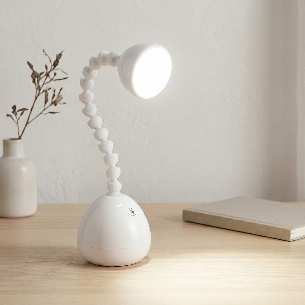 A white LED desk lamp with a unique flexible jointed gooseneck neck illuminating a wooden table next to a book and small vase