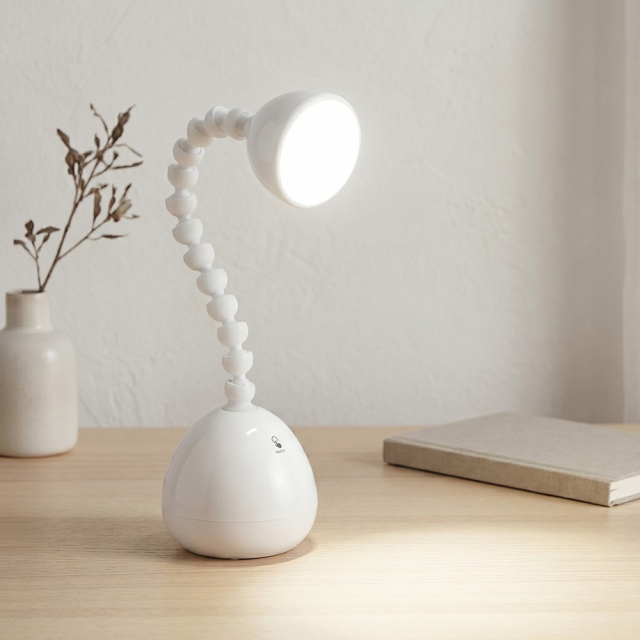 A white LED desk lamp with a unique flexible jointed gooseneck neck illuminating a wooden table next to a book and small vase