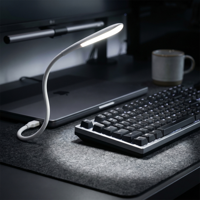 A flexible white USB gooseneck LED lamp illuminating a mechanical keyboard on a desk setup with a laptop and coffee mug in the background