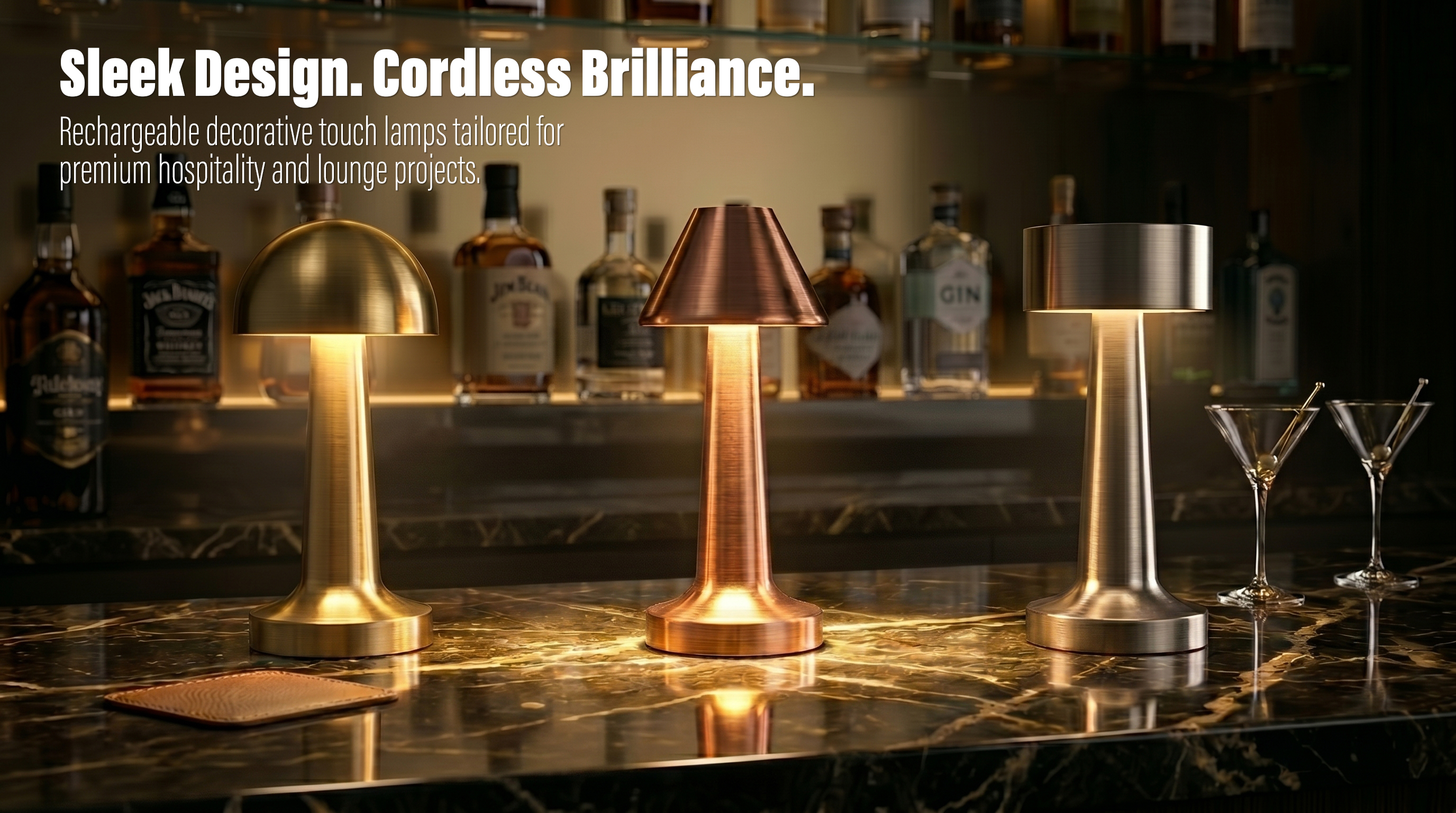 Three modern brushed metal cordless table lamps in gold, copper, and silver finishes illuminated on a marble bar counter with liquor bottles in the background