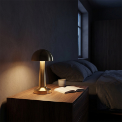A warm dimmable gold bedside night light glowing on a dark wooden nightstand in a cozy bedroom setup