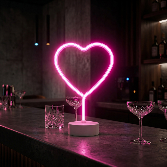 A pink LED heart neon sign standing on a dark bar counter next to crystal cocktail glasses in a lounge ambiance