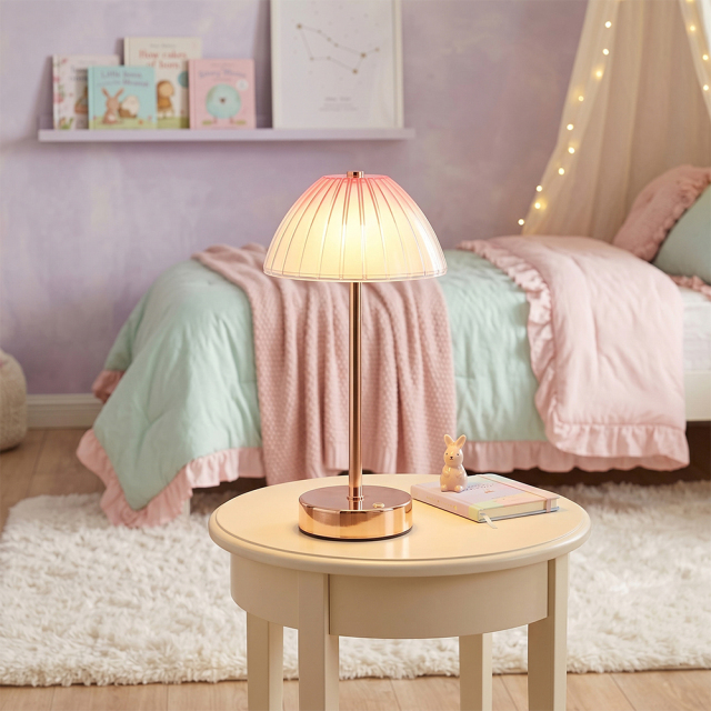 An illuminated cordless umbrella table lamp casting a soft warm glow on a small wooden table in a pastel pink and green bedroom layout