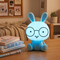 An illuminated light blue cordless rabbit night light glowing with soft blue light on a wooden study table in a bedroom setting