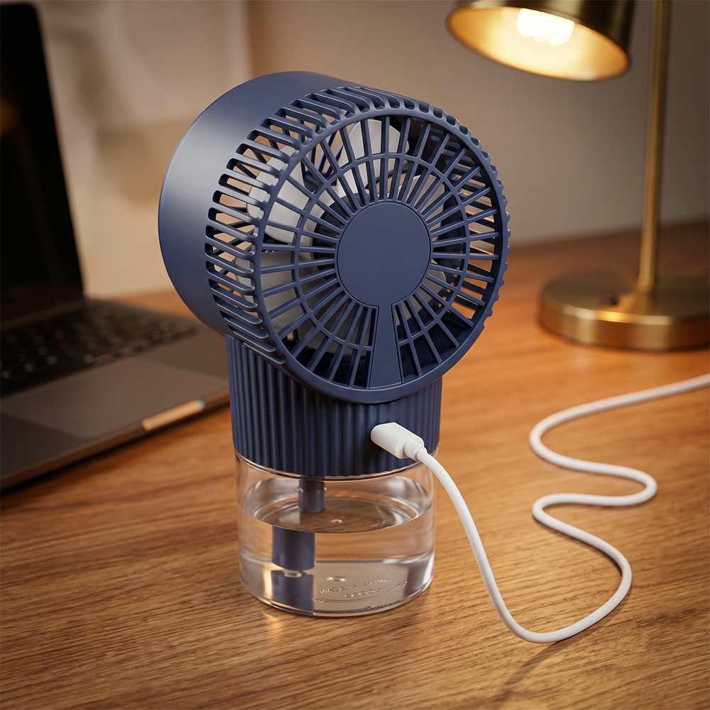 Rear angled view of a dark blue desktop misting fan connected to a white USB charging cable on a wooden desk next to a table lamp