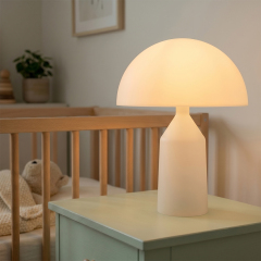 An illuminated white mushroom-shaped night light casting a soft warm glow on a bedside table next to a baby crib