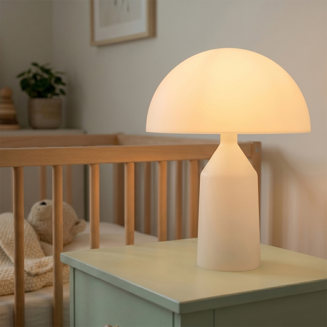 An illuminated white mushroom-shaped night light casting a soft warm glow on a bedside table next to a baby crib